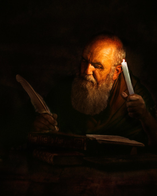 An old man writing a book by candlelight
