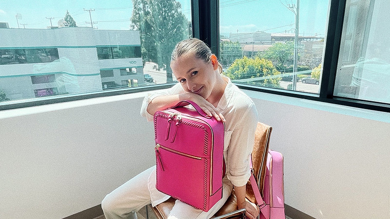 A woman sits in a chair with a pink suitcase on her lap