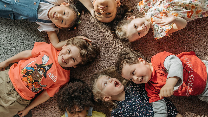 A group of young children led on a carpet smiling and laughing