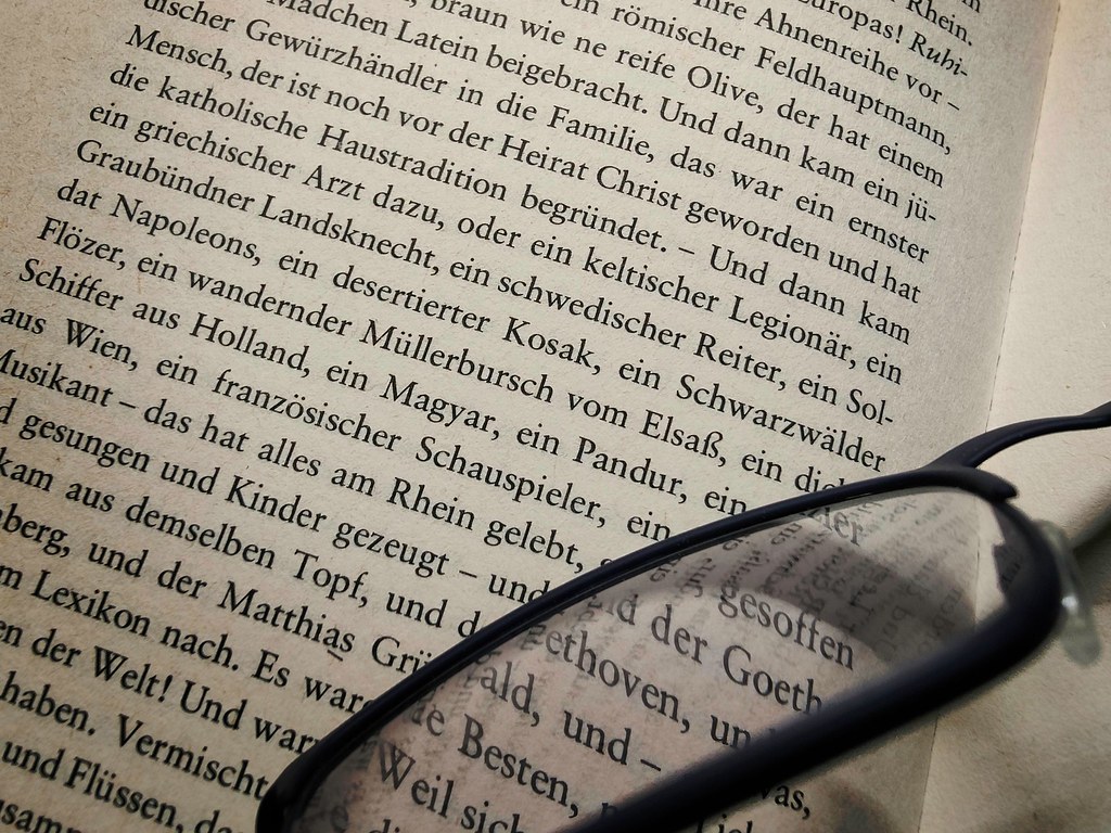 Von der großen Völkermühle - Des Teufels General (aufgeschlagenes Buch mit Tastatur im Hintergrund und aufliegender Brille)