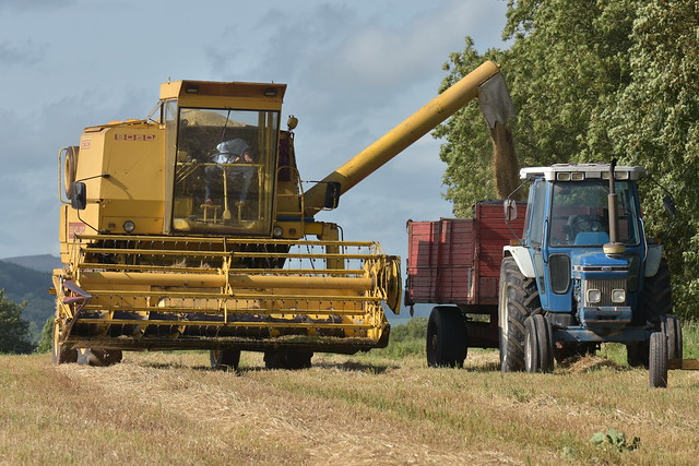 New Holland Clayson 8060 Combine Harvester unloading Spring Barley to a Gran Trailer drawn by a Ford 7610 Tractor