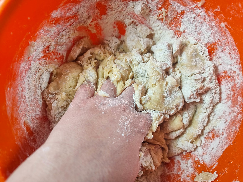 My hand kneading the dough inside the orange bowl.