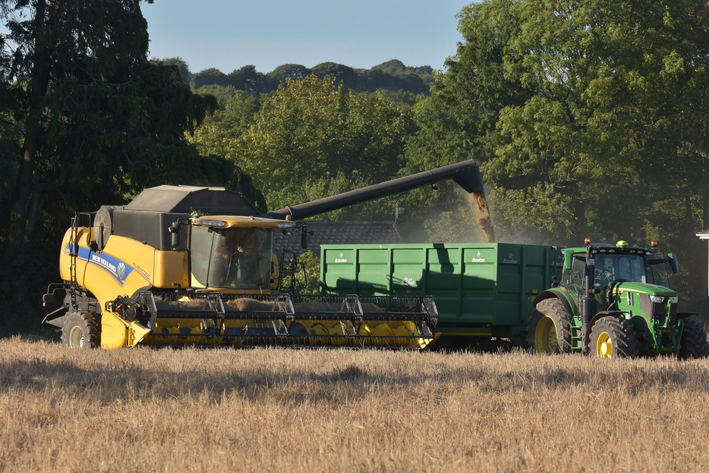 New Holland CX8070 Combine Harvester unloading Spring Barley to a Broughan Engineering Mega HiSpeed Grain Trailer drawn by a John Deere 6R 215 Tractor