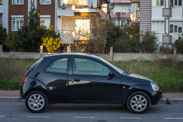 Side, Turkey – February 13 2023:        black  Ford Ka  is parked  on the street on a warm day against the backdrop of a fence, garden