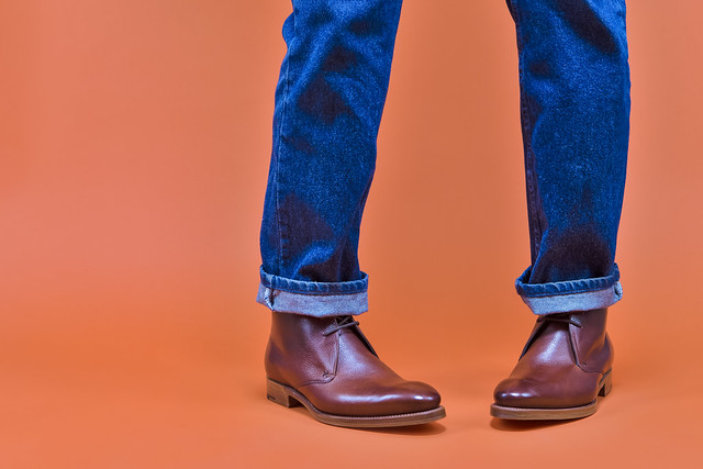 Closeup of Men's Stylish Tanned Leather Brown Brogued Boots On Standing Man Wearing Jeanswera Against Orange Background