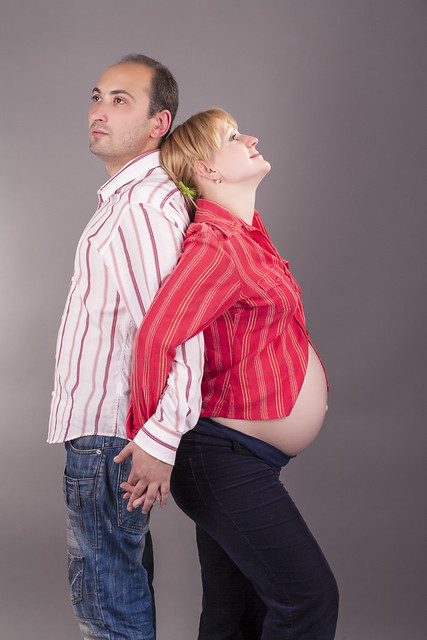 Tranquil Positive Young Couple Standing Together Close While Hugging Her Pregnant Woman And Wearing Casual Clothing Over Gray