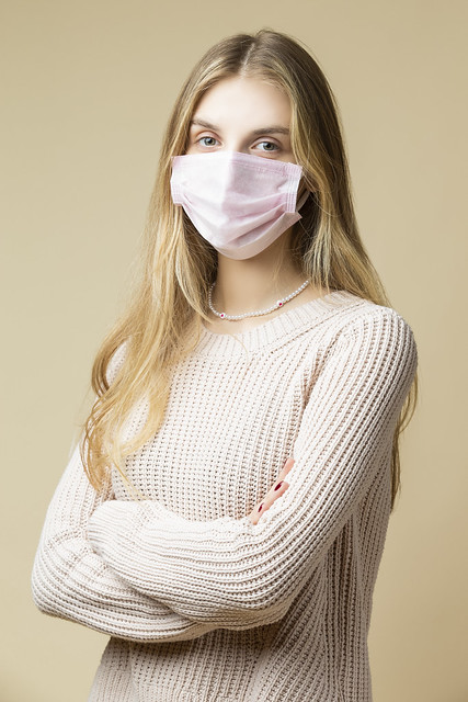 Caucasian Blond Female Girl Wearing Warm Knitted Sweater Using Viral Facial Protective Mask Against Beige.
