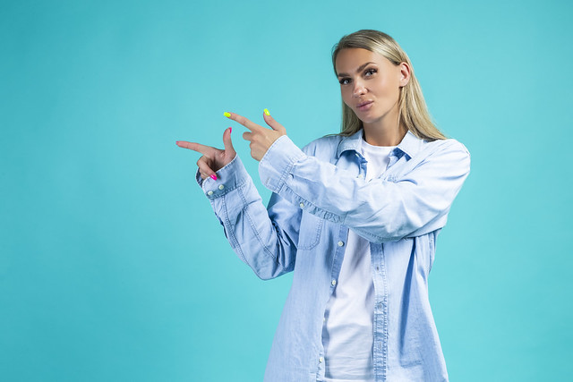 People Emotions and Lifestyle Concept. Winsome Positive Cheerful Young Woman Girl in Casual Blue Jeans Shirt Posing Isolated Over Blue Turquoise Background In Studio While Pointing With Fingers Aside