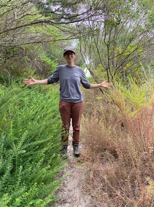 AmeriCorps member treated the invasive plant, lespedeza, with herbicide and shows the impact she made after a week, with one side of the trail showing brown/dead plants and the other side the green invasive plant as it looked before treatment