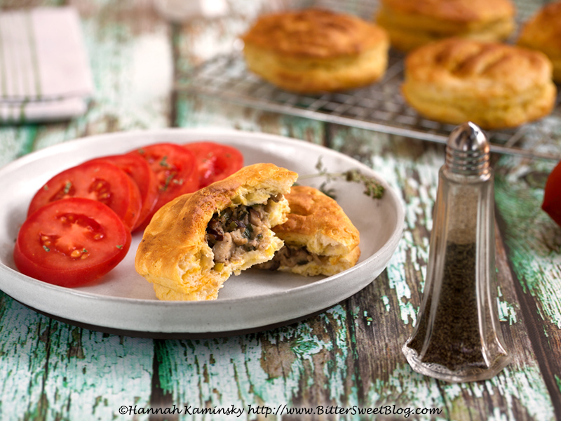 A baked hand pie on a plate with sliced tomatoes, broken in half to show the filling.