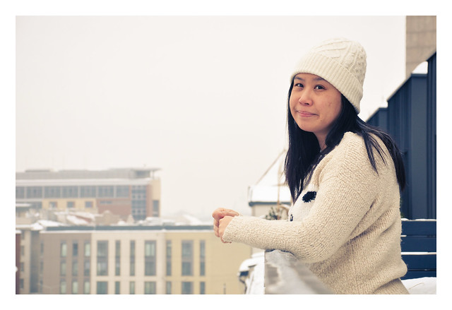 Pretty woman leaning on a metal railing on a balcony in the winter snow with the city below her