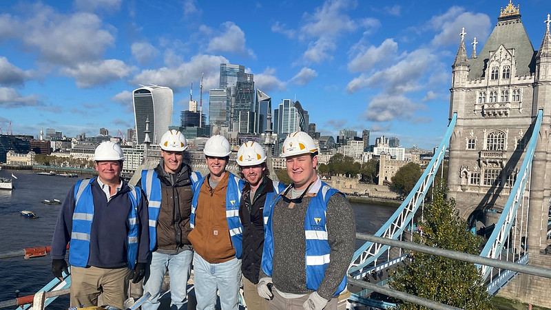 A group of people in blue construction vests poses for a photo in front of the London skyline