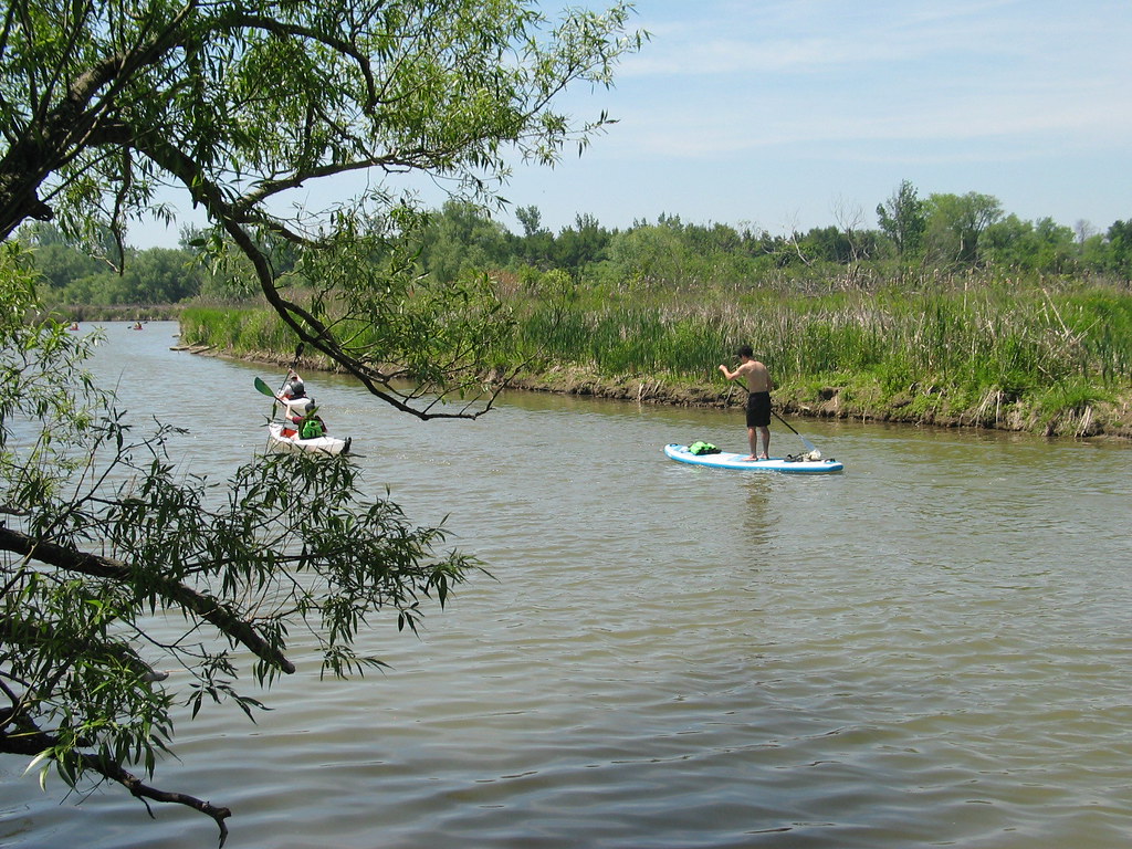 “Three people past us Paddle boarding and kayaking on Duffins creek , while we where walking on a trail at the shore of Duffins creek at noon in Discovery bay , Martins photographs , Ajax , Ontario , Canada , June 6. 2021”