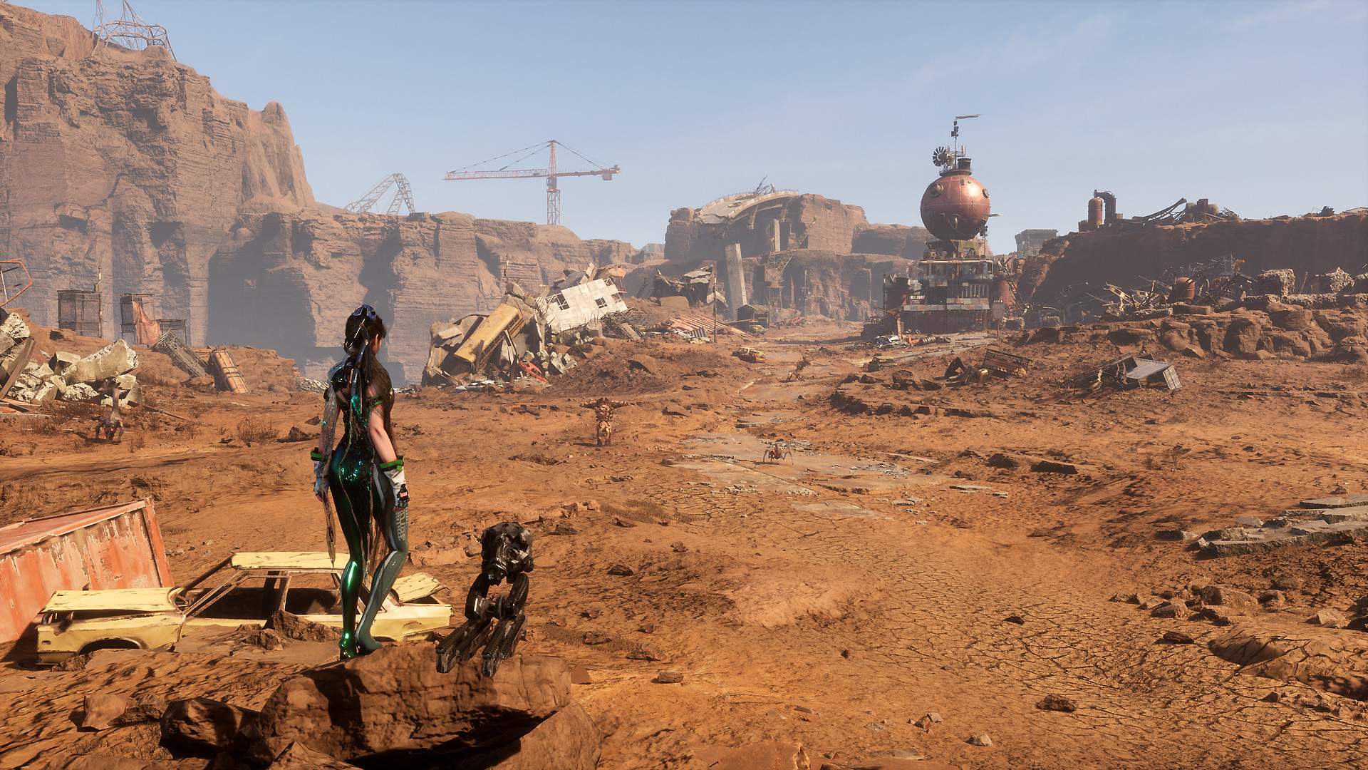 Eve stares out onto a wasteland, littered with destroyed vehicles and containers. Creatures skitter in the open area in front, while cranes can be spotted in the far distance.