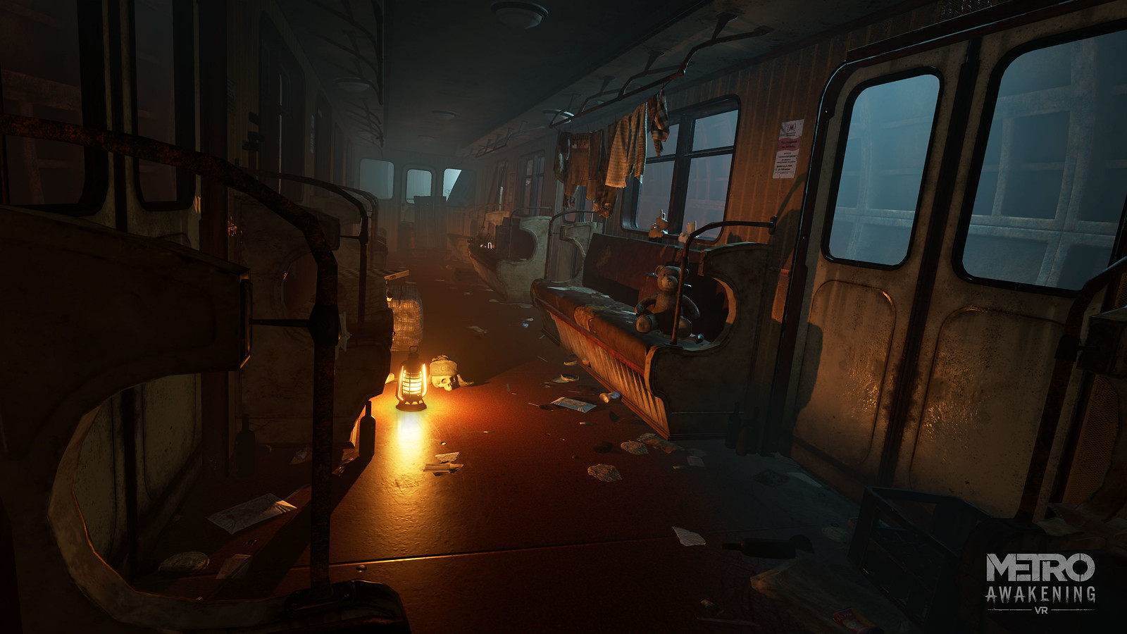 An interior shot of a train carriage, seemingly reappropriated as living quarters, illuminated only be a single lantern left on the floor. A full clothesline stretches across one window, and perched on a seat below is a teddy bear. Cutlery litters the ground, and a human skull, clad in a thick hat, is stationed beside the lantern.