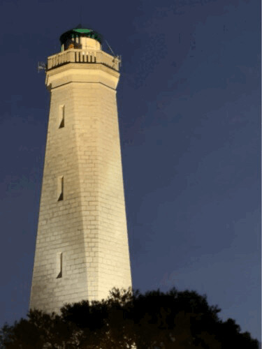 A tall, illuminated white lighthouse against a dark sky near Nice, Provence-Alpes-Côte d'Azur, France, February 2023