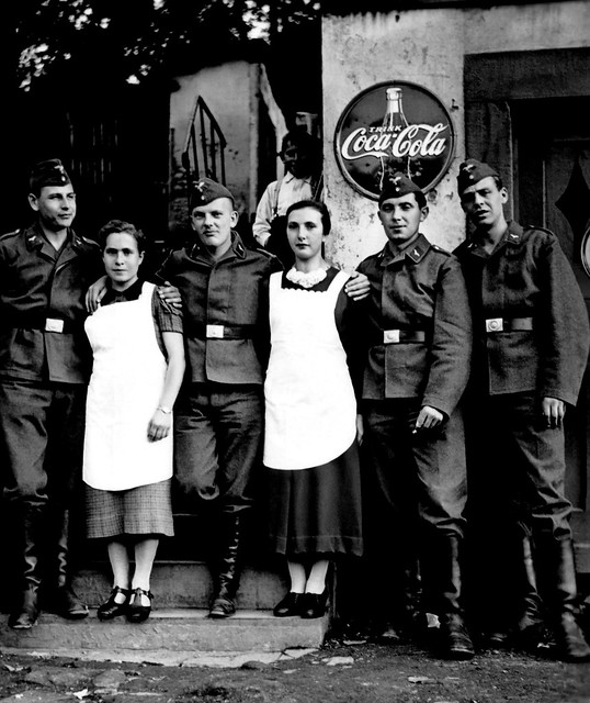 Members of the Luftwaffe and lady friends pose in front of a Coca-Cola sign in Germany circa WW2