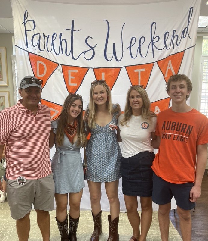 A group of people stand in front of a Parents Weekend sign.