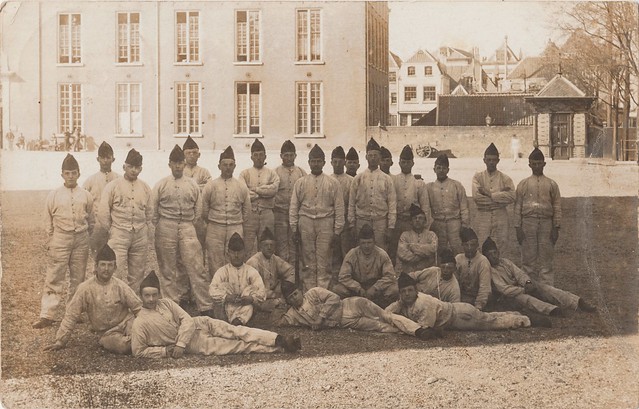 Fotokaart - Groep militairen poseert in de schaduw op het Kazerneplein, de Willemskazerne op de achtergrond (poststempel 1909 verstuurd naar Hoogblokland, Bikker, Slob)