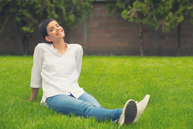 Smiling girl sitting on the grass of home garden on sunny spring day
