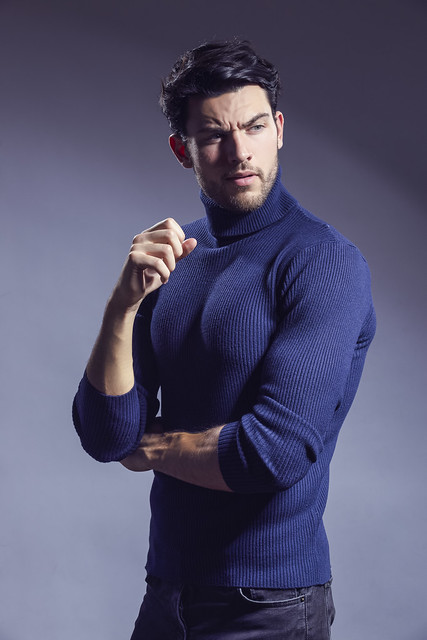 One Handsome Caucasian Brunet Businessman Wearing Sweater Posing With Folded Hands Looking Aside Against Gray Background.