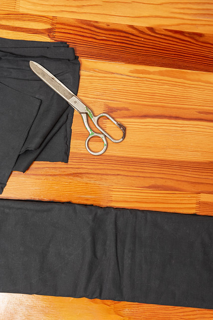 Tailoring Concepts. Cutting Textile Cloth at Work Table With old Rusty Scissors and Black Fabric