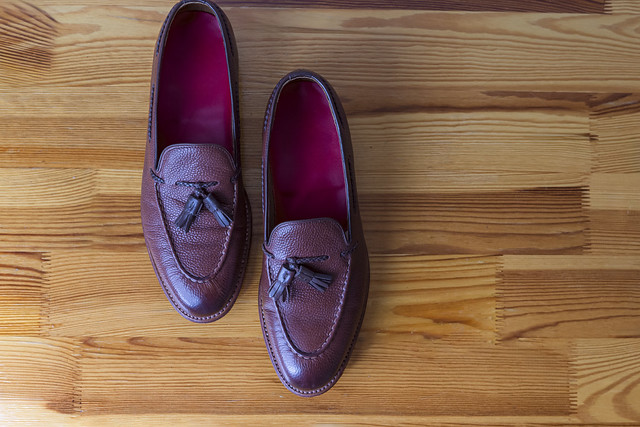 Closeup Upper View of Pair of Traditional Formal Stylish Brown Pebble Grain Tassel Loafer Shoes On Wooden Surface.