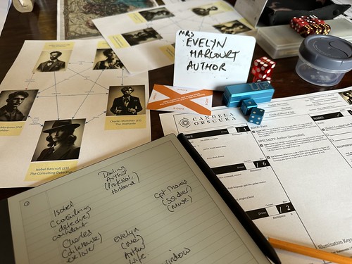 A picture of the game table in front of me in the Candela Obscura game, with a character name tag ('Mrs Evelyn Harcourt, Author'), a relationship map, X-card and a reMarkable. There's also a character sheet and lots of six-sided dice.
