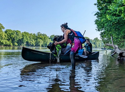 woman picking up trash out of the water next to a canoe