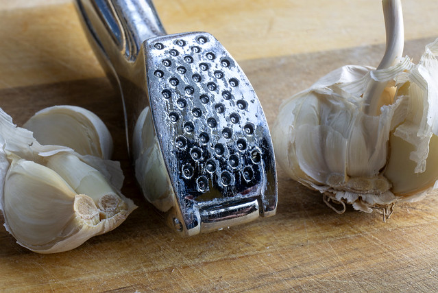 Close up of a steel garlic press and fresh garlic