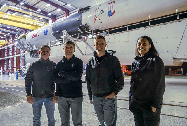 The crew members of NASA's SpaceX Crew-8 mission pose for a photo in front of the assembled Dragon spacecraft and Falcon 9 rocket in the hangar at Launch Complex 39A. From left to right are Mission Specialist Alexander Grebenkin, Pilot Michael Barratt, Co
