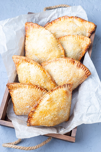 Small peach and cinnamon hand pies with crust dough,  sprinkled with sugar, on wooden tray, vertical, top view, closeup