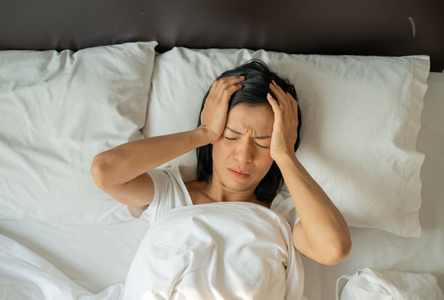 Unhappy exhausted mature woman with closed eyes lying in bed, touching temples close up, tired female suffering from headache or migraine, feeling unwell, suffering from insomnia, lack of sleep
