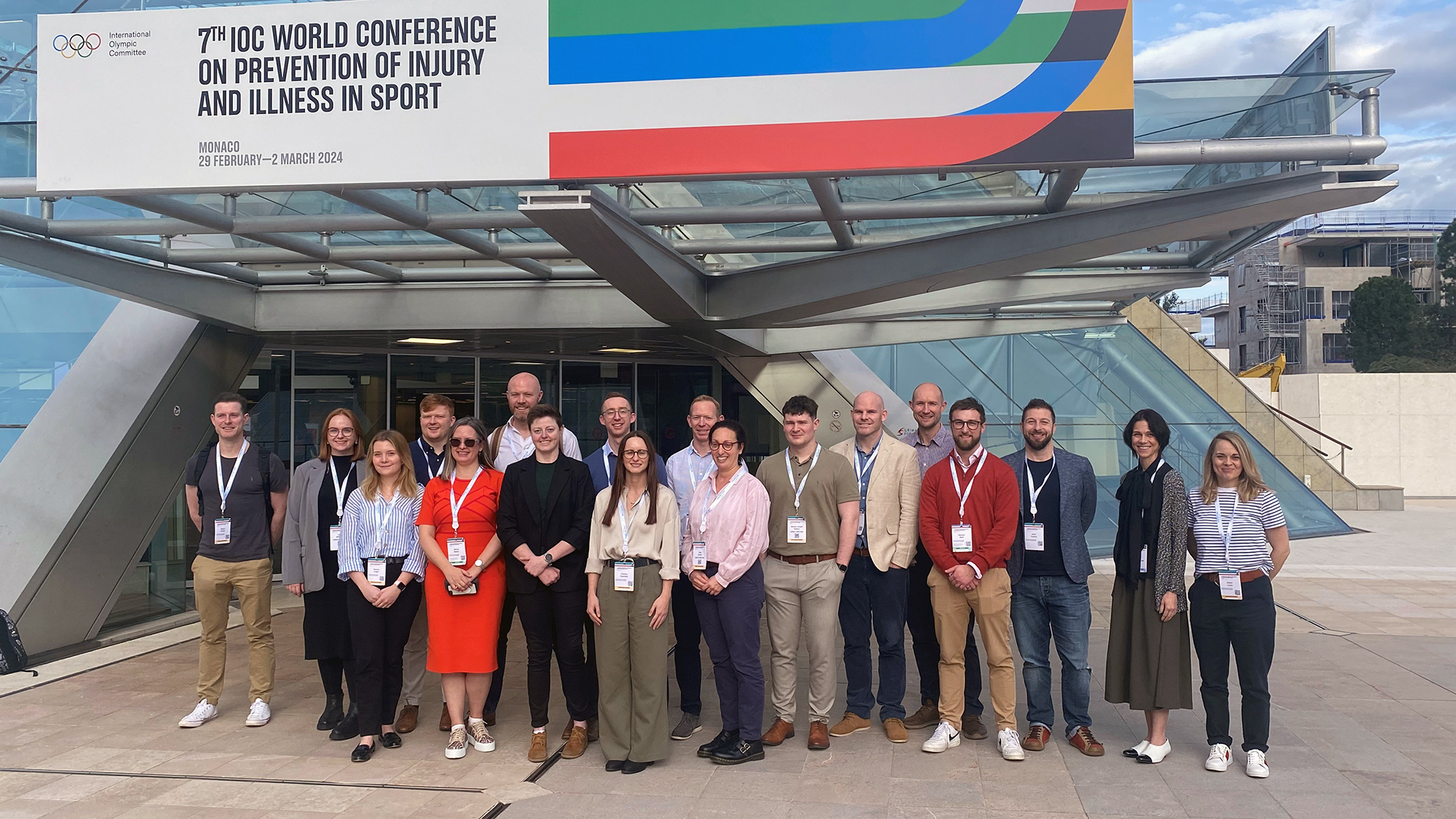 A group of people stood outside a building with an 'IOC World Conference on Prevention of Injury and Illness in Sport' sign on it.