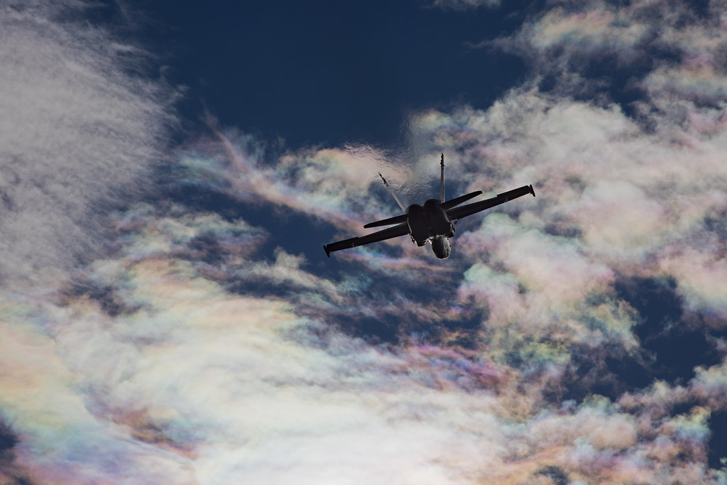 F/A-18 Hornet flies under iridescent clouds