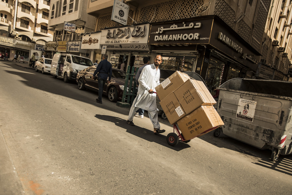 Muž s vozíkem na ulici v Dubaji--Man walking down the street of Dubai carrying boxes on a hand cart, UAE