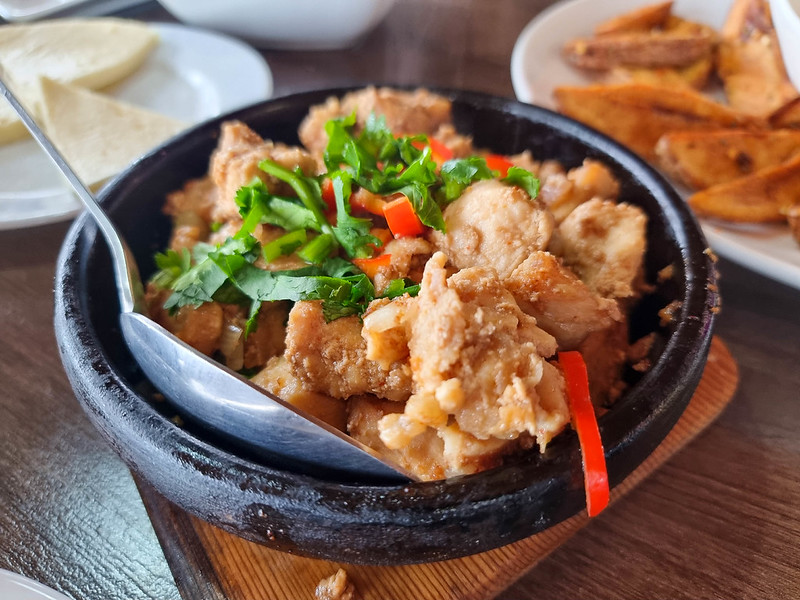 A black bowl with fried pork, decorated with chopped red peppers and greens.