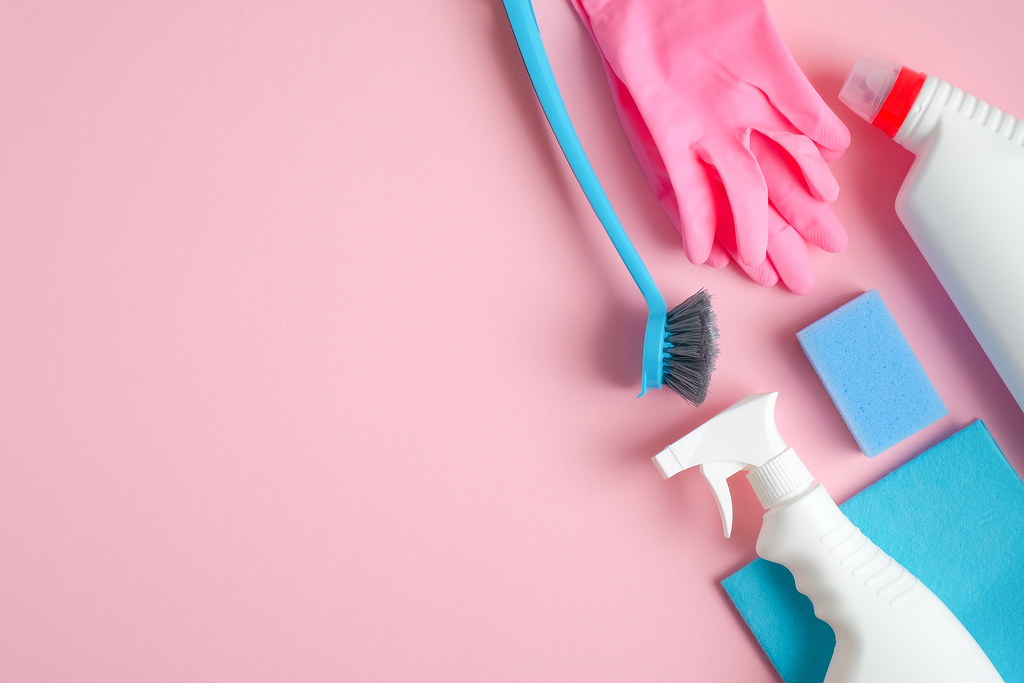 House cleaning tools and cleaning products on pink background. Top view blue sponge, gloves, brush and cleaner bottles. Cleaning services concept.