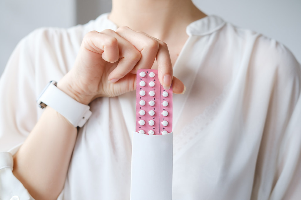 Unrecognized woman in white blouse holding hormonal oral contraceptives in a pink blister. Concept of Hormonal methods of birth control. Estrogen and Progestin hormonal balance.