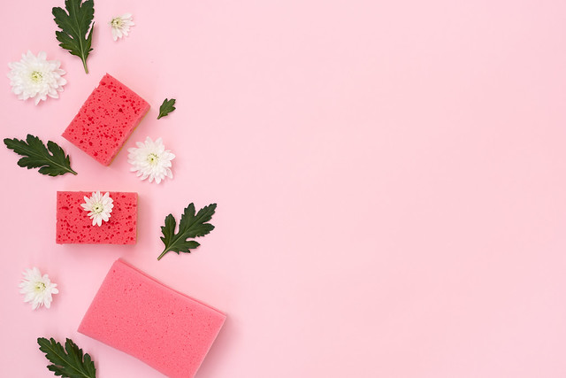 Pink cleaning sponges, white flowers and green leaves on pastel background