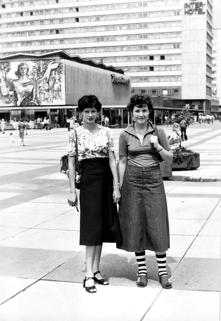 Two young women pose in front of the “Interhotels Prager Straße” hotel and restaurant complex in Dresden, Communist East Germany 1972
