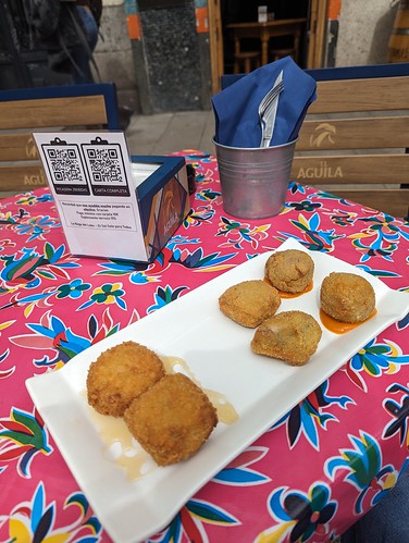 Six croquetas on a white plate on top of a colorful tablecloth