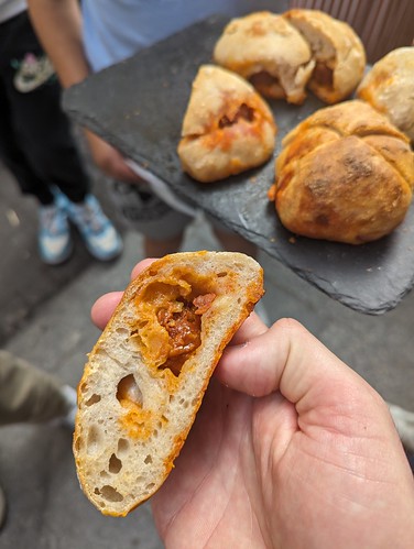 A closeup of a hand holding an empanada filled with meat and cheese. Blurred in the background is a serving platter with more empanadas