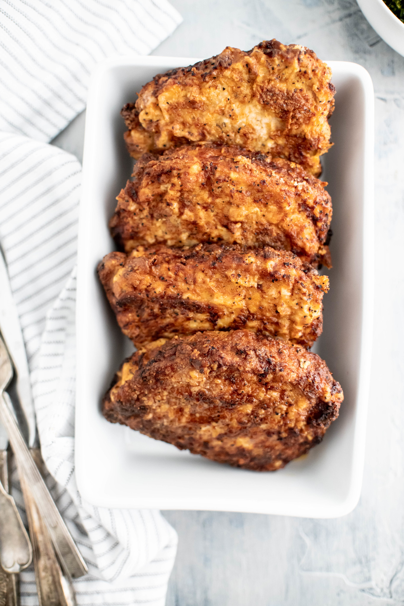 Four fried pork chops lined up in a white rectangular dish.