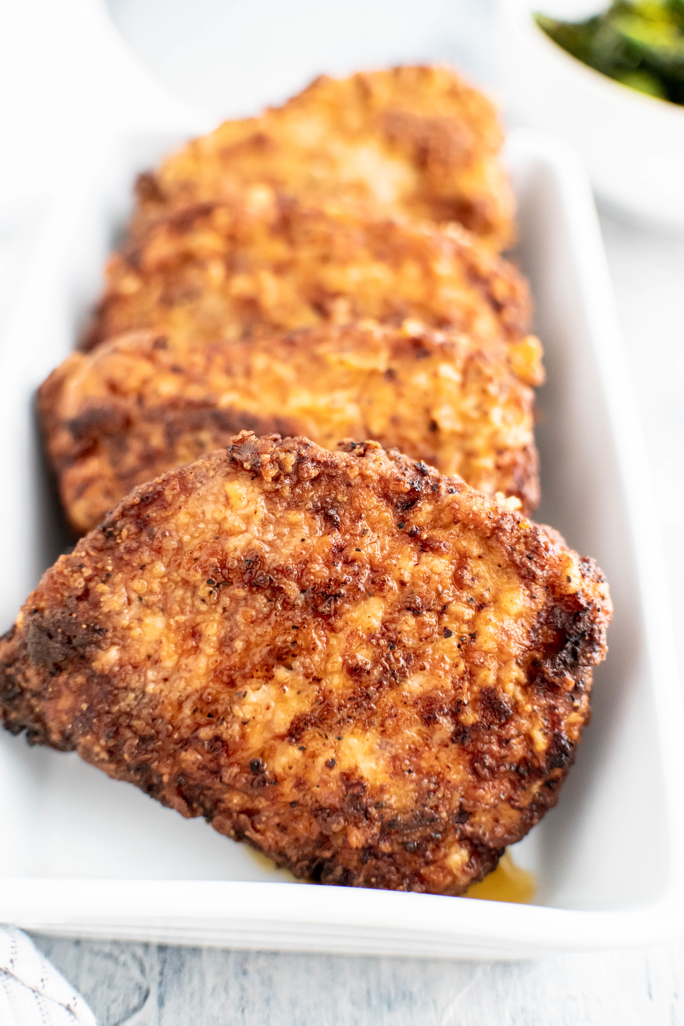 Close up of four southern fried pork chops lined up in a white rectangular dish.