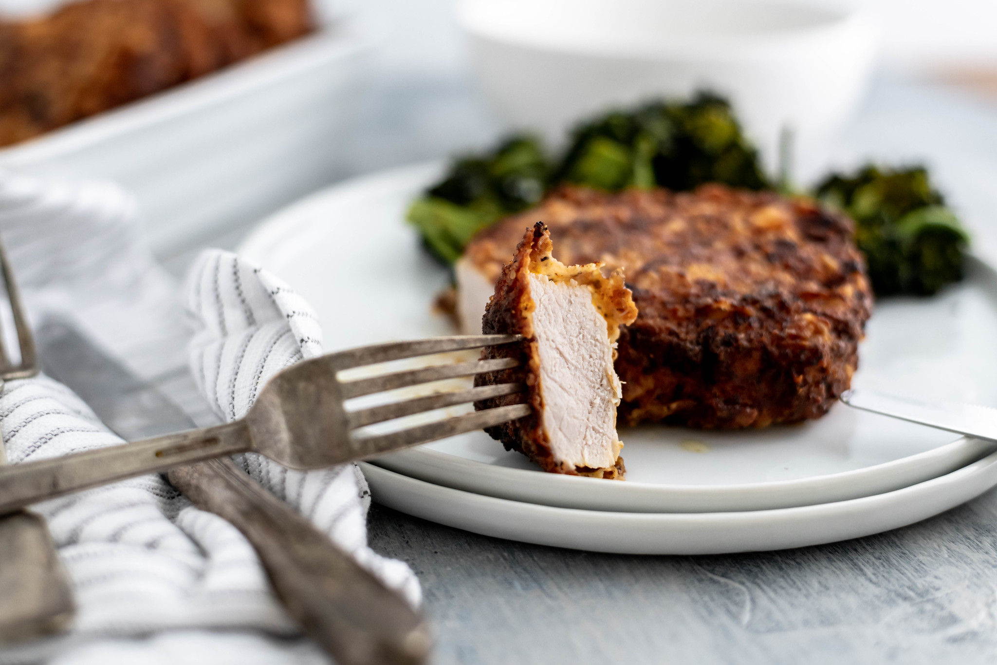 Bite cut out of a southern fried pork chop on a white round plate with roasted broccoli on the side.