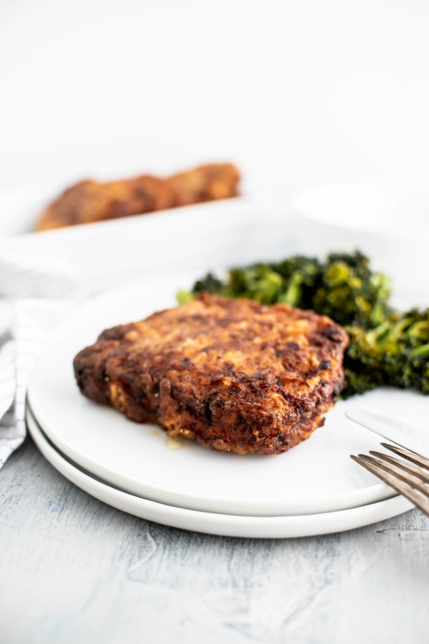 Fried pork chop and roasted broccoli on a white round plate.