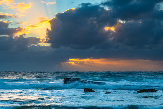 Moody sunrise seascape with clouds and sunrays at the rocky inlet