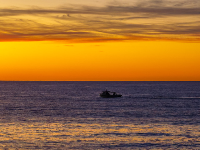 Sunrise at the seaside with high cloud and boats checking the nets