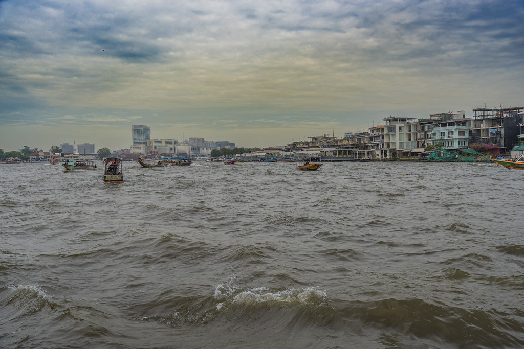 Busy Chao Phraya river with many boats under a cloudy sky in Bangkok, Thailand